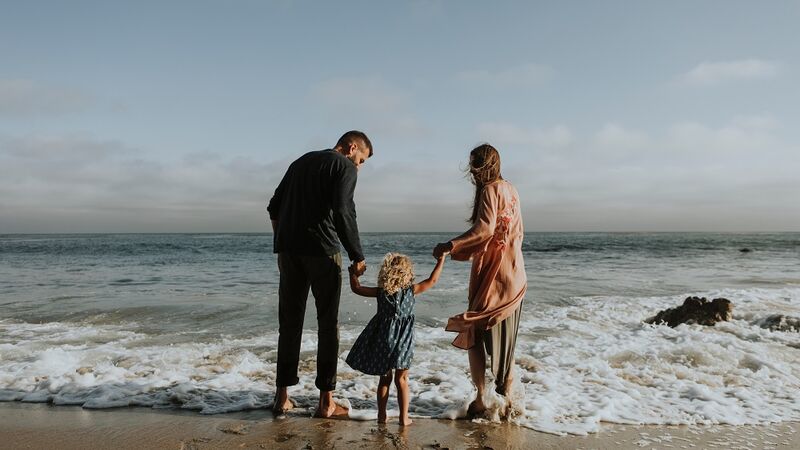 Kleine Familie barfuß am Strand und in den Wellen